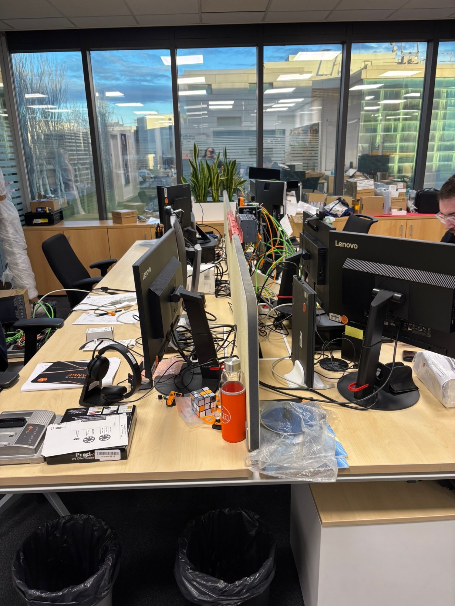 Oficina moderna con escritorios, monitores y vegetación visible al fondo.