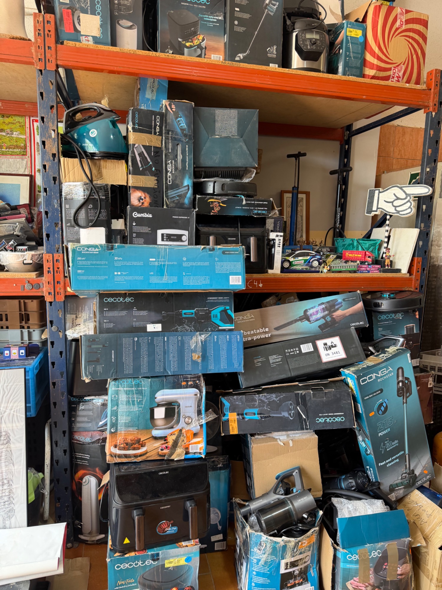 Estante desordenado con productos electrónicos y herramientas en cajas.